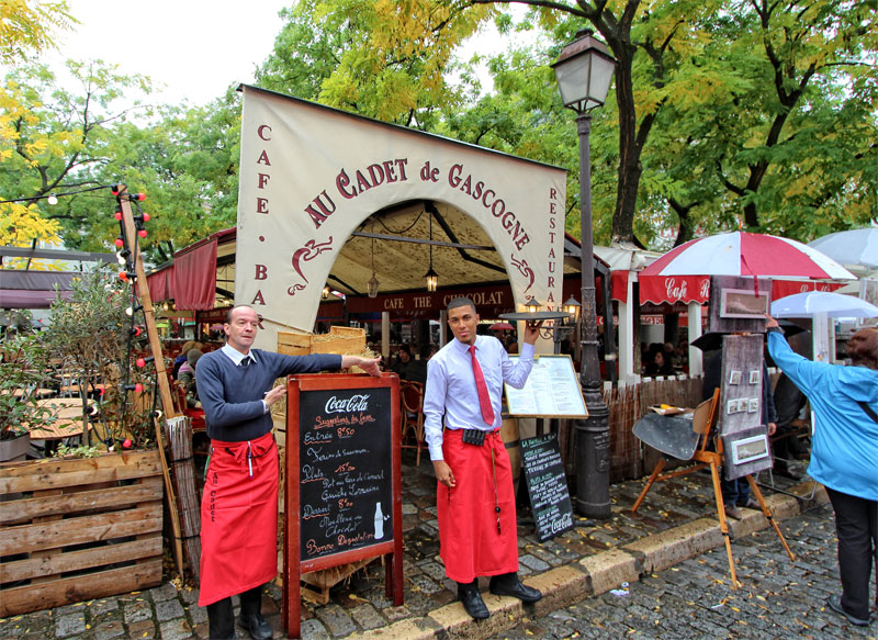 Two waiters with red aprons tempt passers by to a pretty restaurant in Montmartre Paris