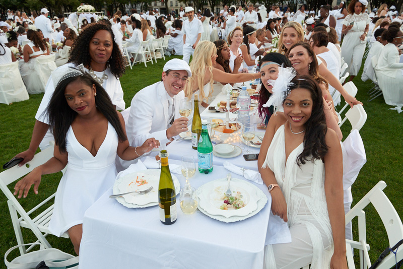 Comensales sonrientes vestidos de blanco para el picnic Diner en Blanc Paris