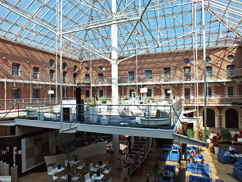 Barra de champán de cristal suspendida bajo un techo de cristal que cubre un patio de una abadía en Lille